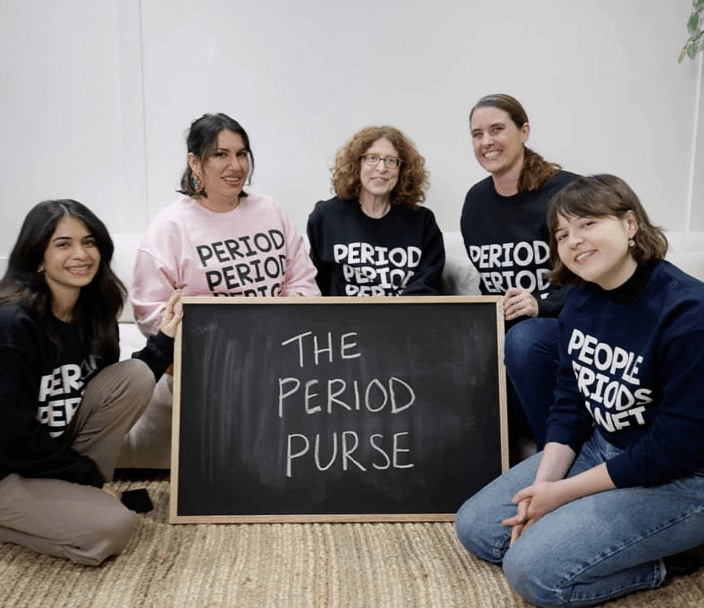 Women wearing a shirt that says Period, sitting around a blackboard with the words The Period Purse