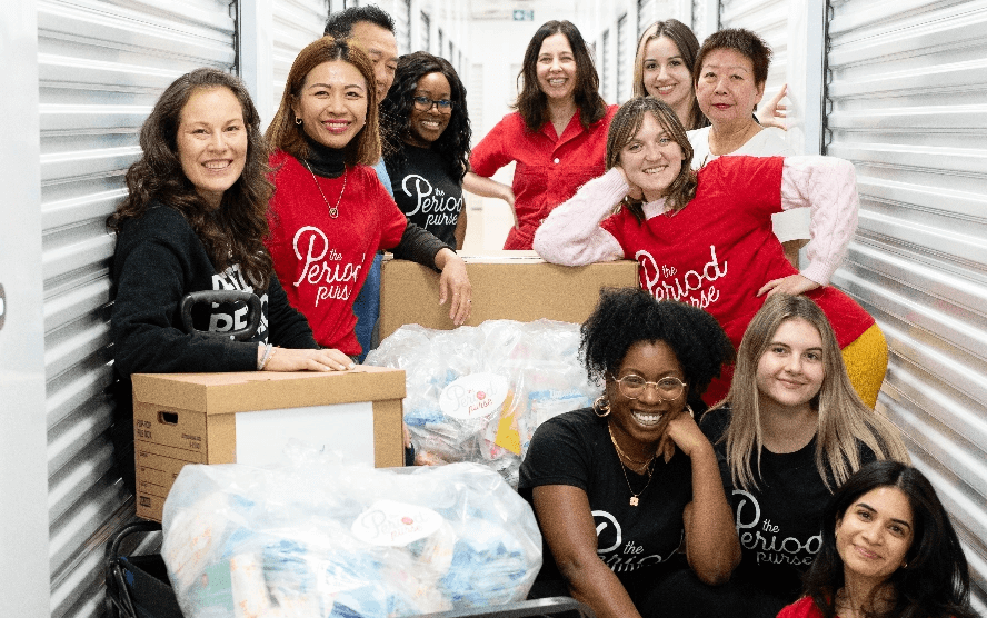 Volunteers posing and smiling in front of a camera, and showing many donated products nearby
