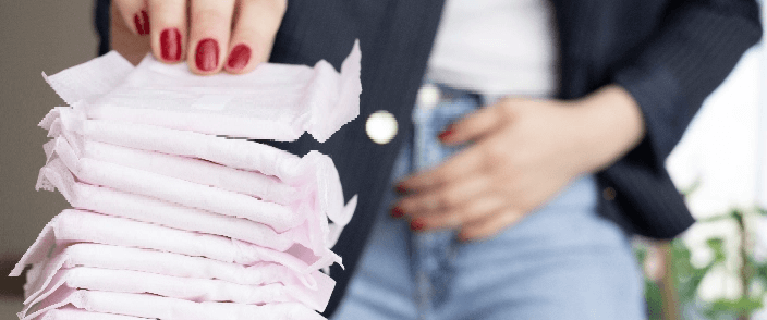 A woman holding her belly and picking up a tampon pack.