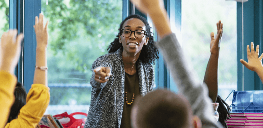 A female staff pointing to enthusiastic students raising hands