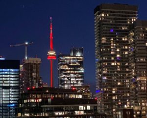 Toronto skyline at night featuring the CN Tower illuminated in red, surrounded by high-rise buildings.