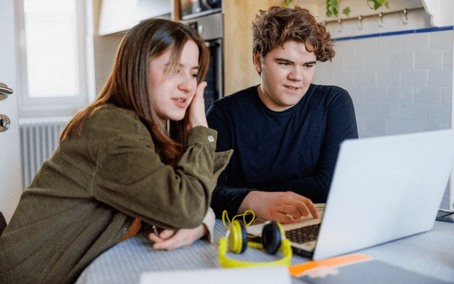A teenage girl and boy watching a laptop screen together