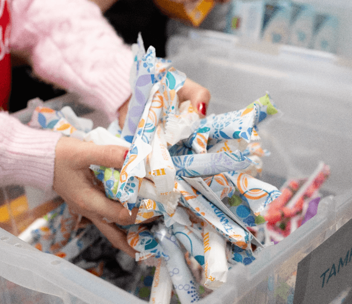 Hands putting sealed tampons into a donation box