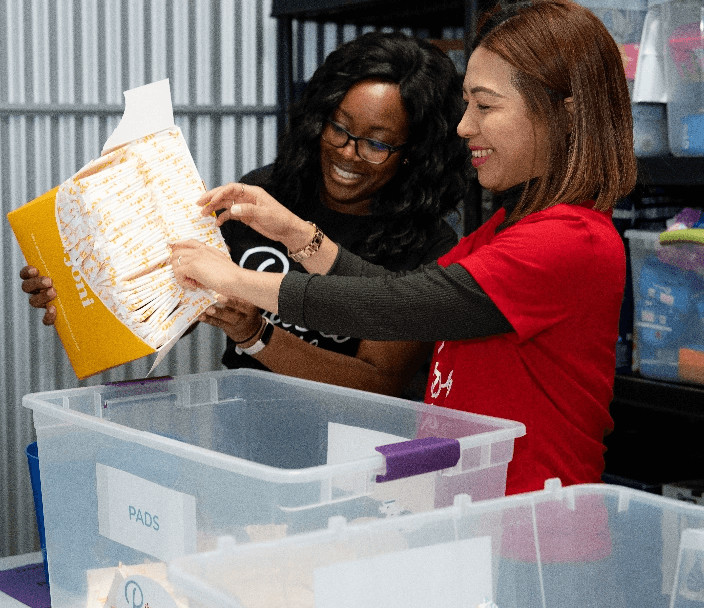 A woman smiling and putting a box full of pads into a container labelled Pads