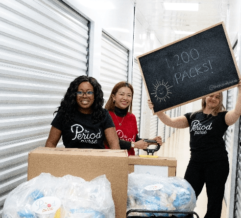 Staff members carrying a box and another member holding up a blackboard with words 1200 packs!