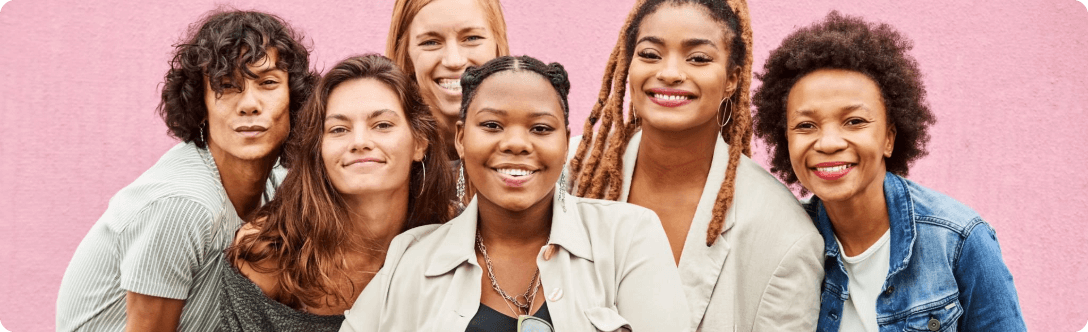 A diverse group of women smiling on a pink background