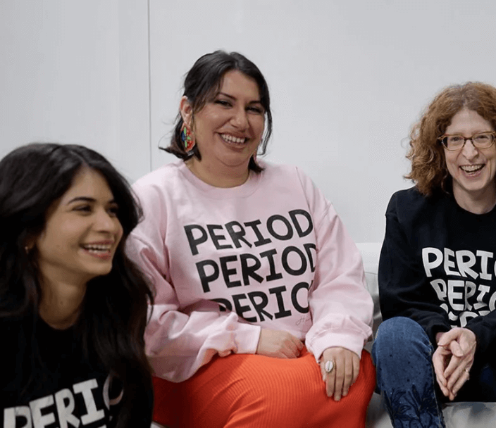 Three smiling women wearing T-shirt with word Period