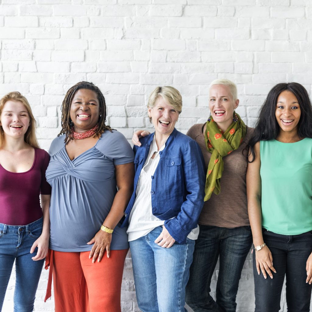 Group of Women, standing in front of a white brick wall, smiling